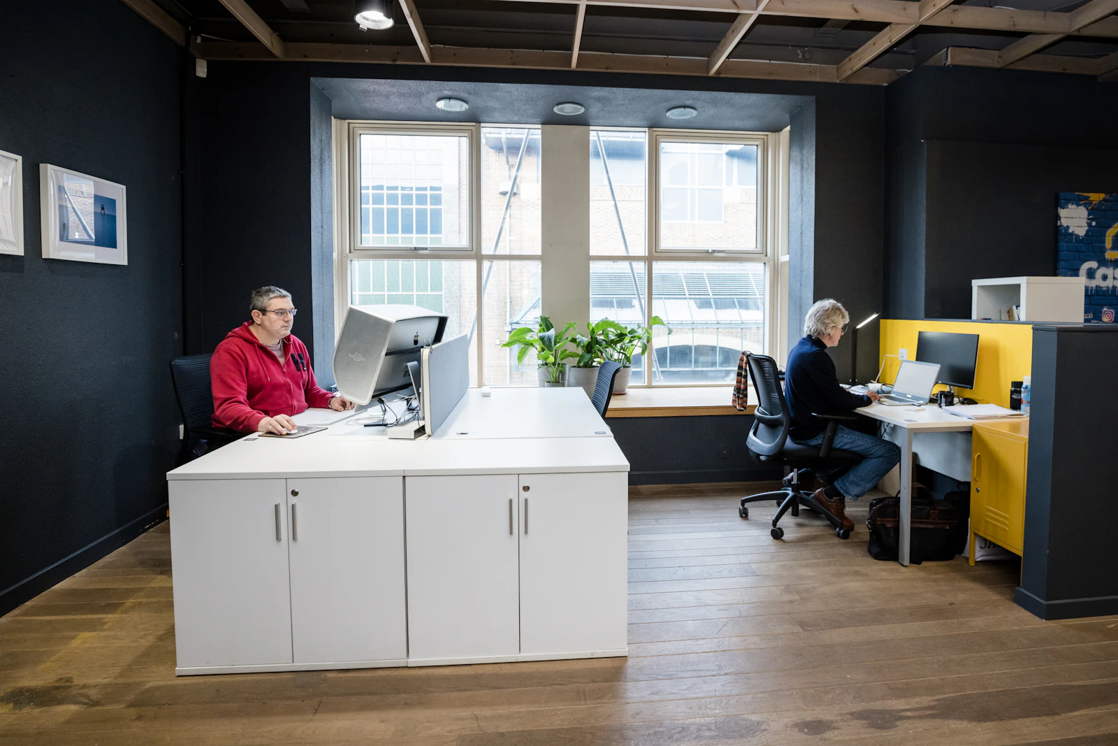 People working in a shared office Two people working at desks in a bright shared office with large windows